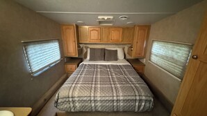 Une chambre compacte dans un camping-car, comprenant un lit, des placards en bois et une petite table de chevet.