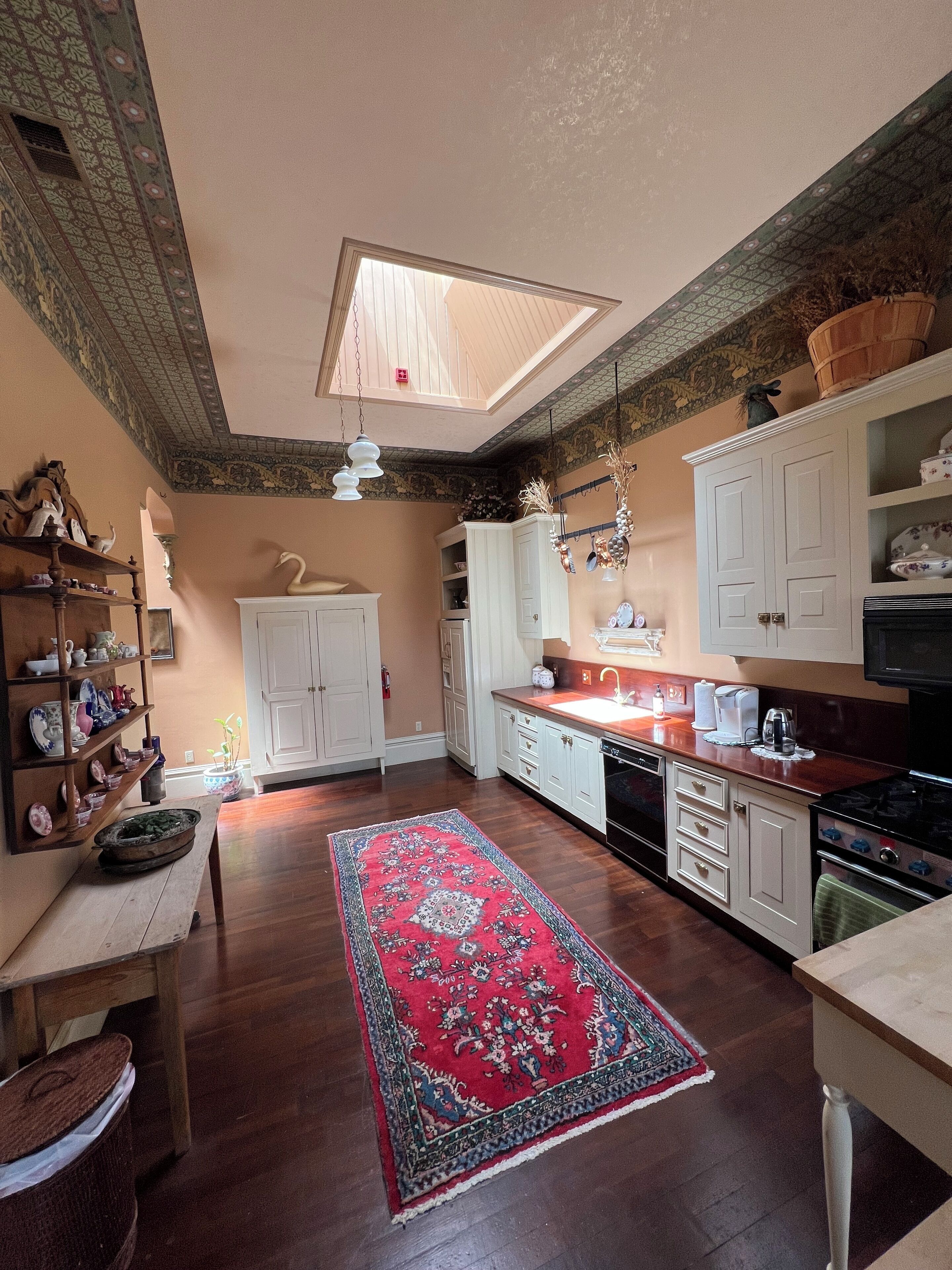 A spacious kitchen with wooden cabinets, a central island, and a red patterned rug.