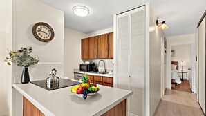 Une cuisine moderne avec des meubles en bois, un plan de travail blanc, un panier de fruits, une bouilloire et un four à micro-ondes.