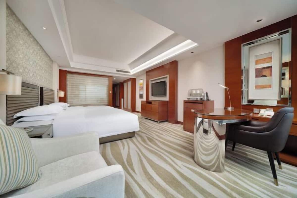Una habitación de hotel con cama, escritorio, silla, televisor y un amplio ventanal.