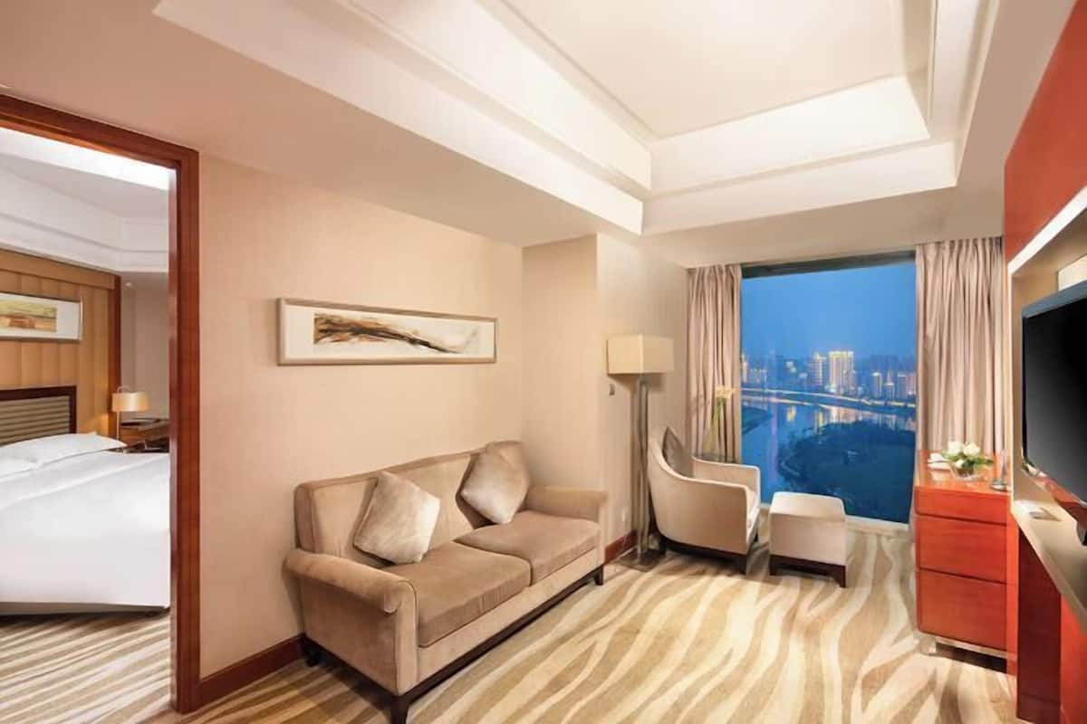 Habitación de hotel con cama, sofá, televisión, escritorio y vistas a la ciudad.
