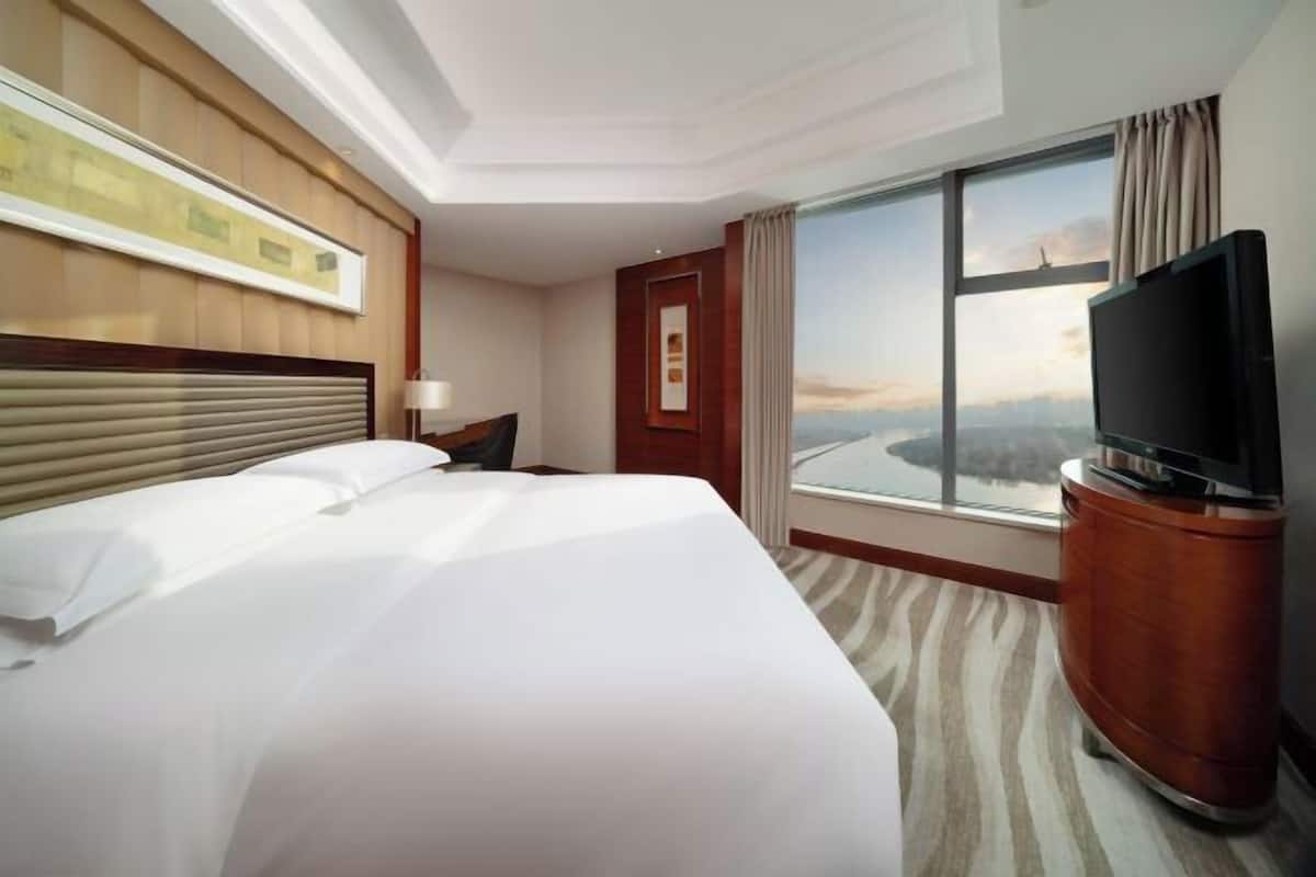 Una habitación de hotel con una cama grande, un televisor sobre un mueble, una ventana con vistas y un cuadro en la pared.
