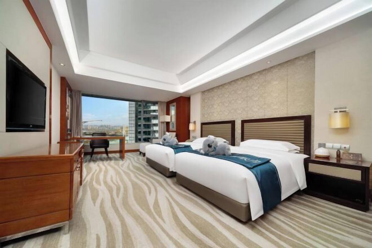 Habitación de hotel con dos camas, un escritorio, una silla, un televisor y vistas a la ciudad.