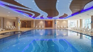 Una piscina interior de diseño moderno, con un área de natación central y sillones de descanso alrededor del borde.