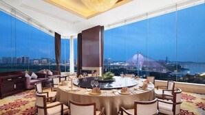 Un comedor lujoso con una mesa redonda para seis personas, ventanas amplias que ofrecen vistas a la ciudad y un candelabro colgante.