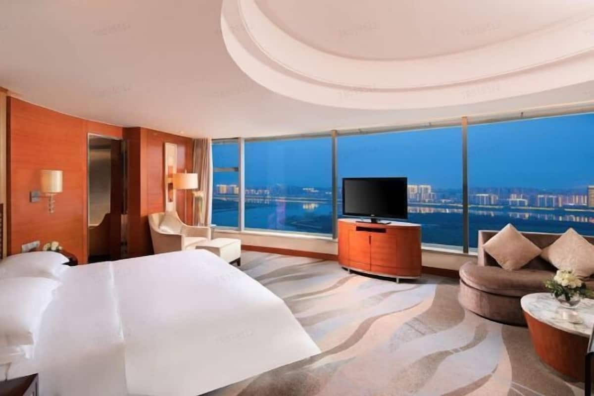 Habitación de hotel moderna con una cama grande, un sofá, un televisor y vistas a un paisaje urbano.