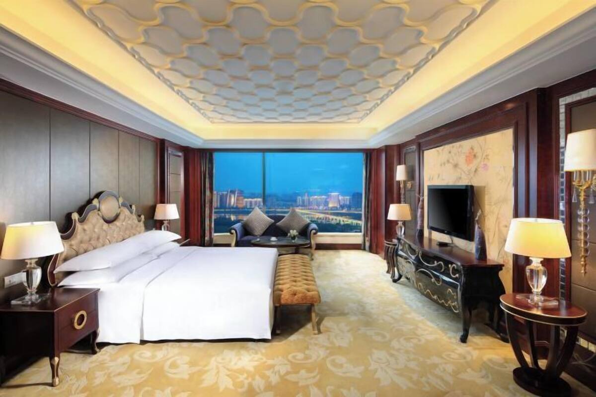 Habitación de hotel con una cama grande, un sofá, un televisor y vistas a un paisaje urbano.