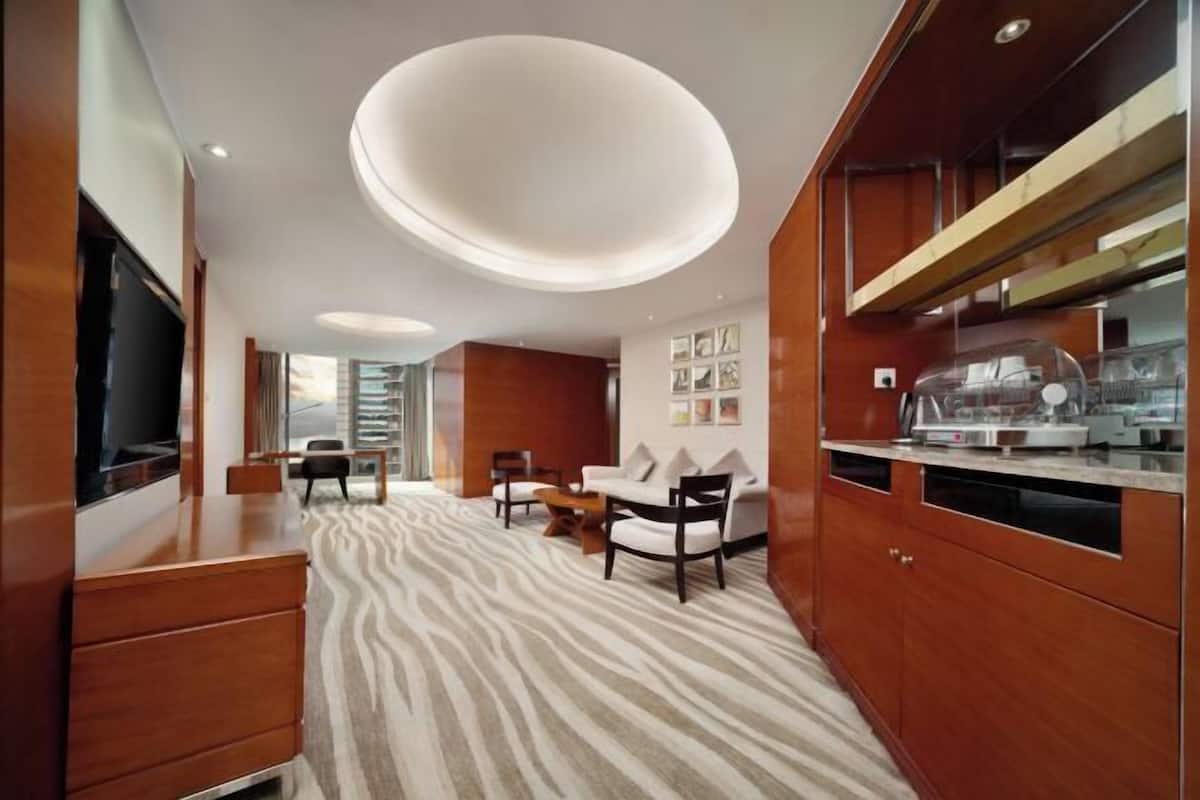 Una habitación de hotel moderna con una cama grande, un aparador de madera, un televisor de pantalla plana, una zona de comedor con mesa y sillas, y una cocina con encimera y electrodomésticos.