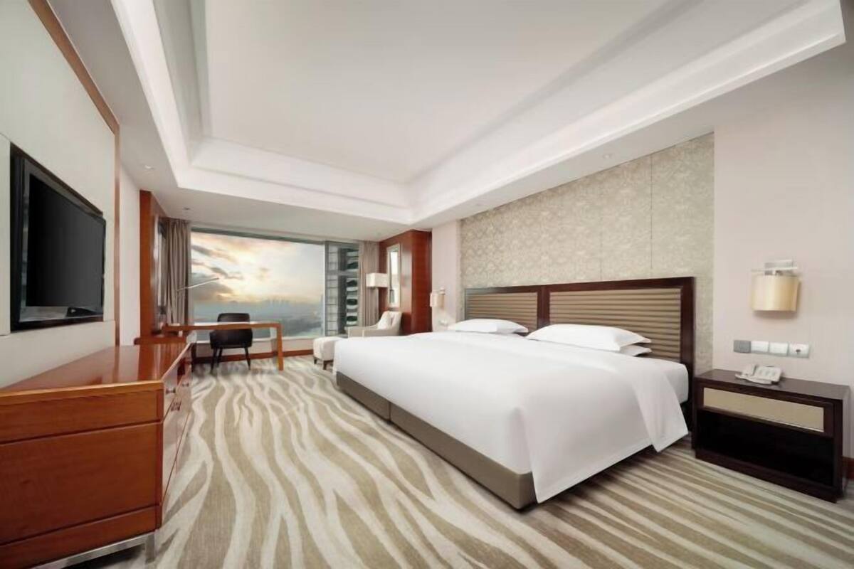 Habitación de hotel con una cama grande, un escritorio con silla, televisor y mesita de noche con teléfono.
