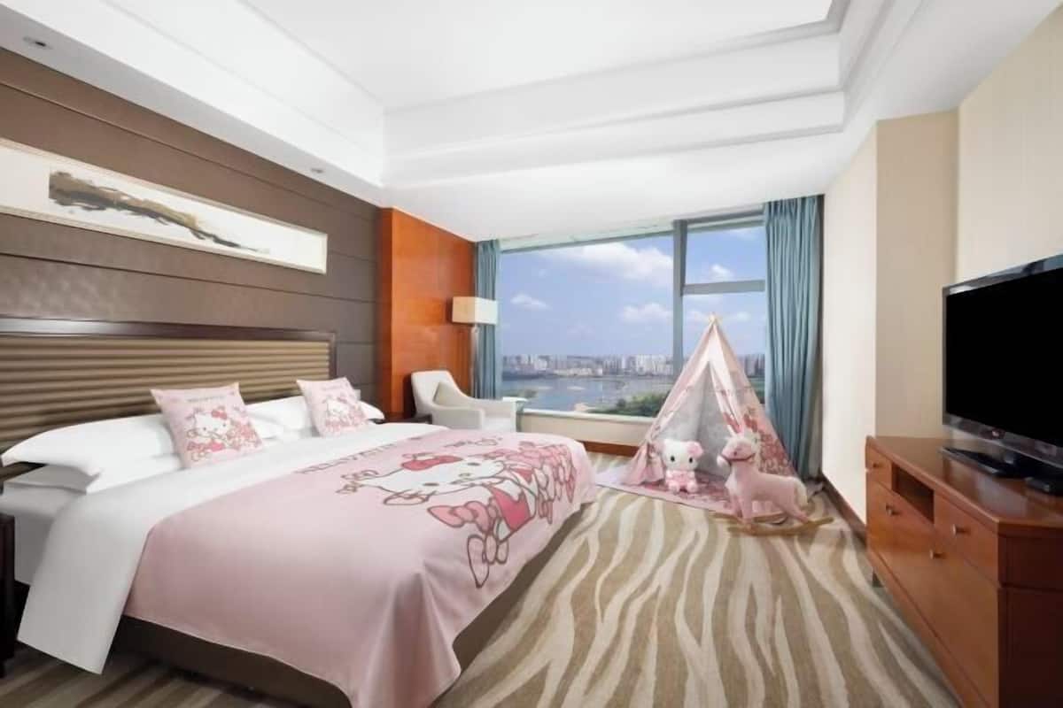 Habitación de hotel con cama, televisión, ventana con vista a la ciudad y una estructura similar a una tienda de campaña con un peluche.