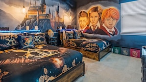 Un dormitorio con un gran mural de un castillo, dos camas con ropa de cama temática y una ventana con persianas.