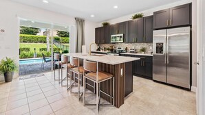 Una cocina moderna con gabinetes oscuros, electrodomésticos de acero inoxidable y una isla grande con taburetes de bar.