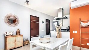 Un comedor con una mesa y sillas blancas, un aparador de mimbre y un espejo decorativo en la pared.