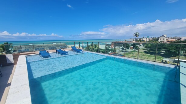 A clear blue pool with lounge chairs, overlooking a beach and ocean. - Flat Térreo 02 Jardim by La Playa (Ipojuca)