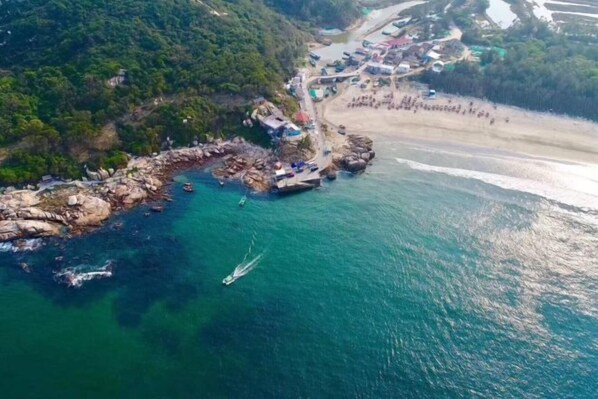 An aerial view of a coastal area with rocky terrain, a beach, and several boats. - Hilton Hotel (Taishan)