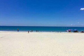Una spiaggia con cielo sereno, una riva sabbiosa e alcuni ombrelloni.