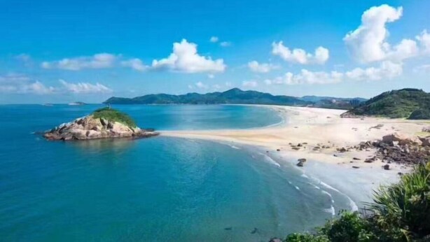 A coastal landscape with a sandy beach, clear blue waters, and distant mountains. - Hilton Hotel (Taishan)