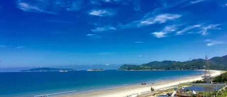A coastal hotel with a beach view, a promenade, and a clear sky.