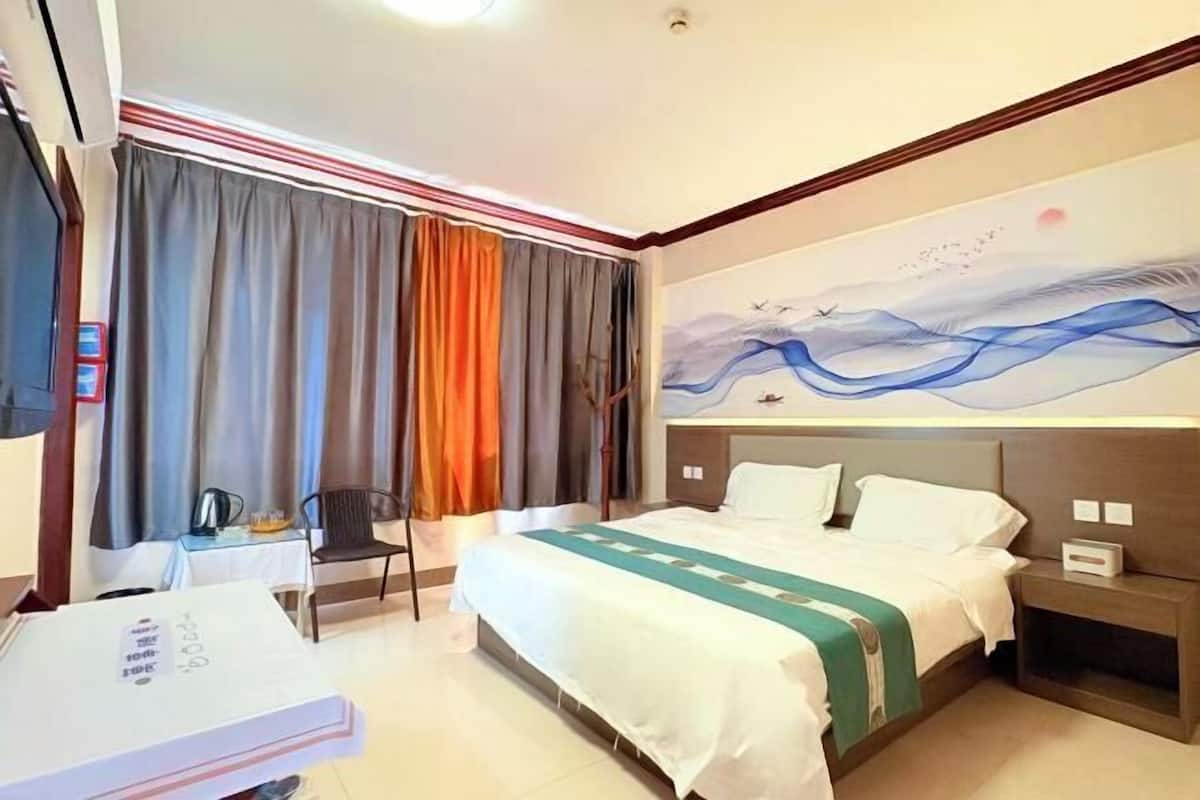A hotel room with a bed, a desk with a chair, a painting on the wall, and curtains.