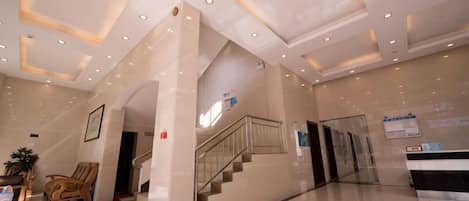 A hotel lobby with a reception desk, a staircase, and a red carpet.
