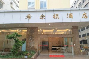 A hotel entrance with a clear glass facade, a reception desk, and a small outdoor garden area. - Hilton Hotel (Taishan)
