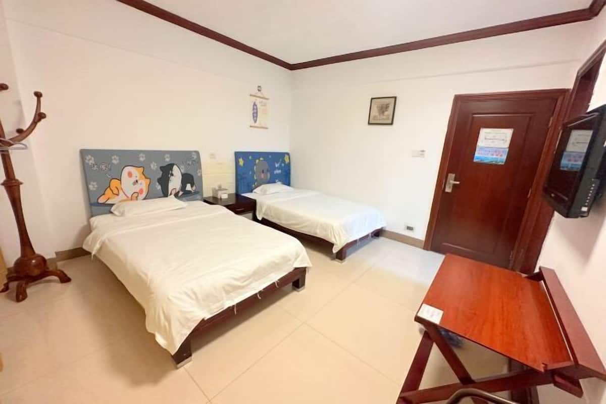 A hotel room with two beds, a wooden chair, a TV, and a coat rack.