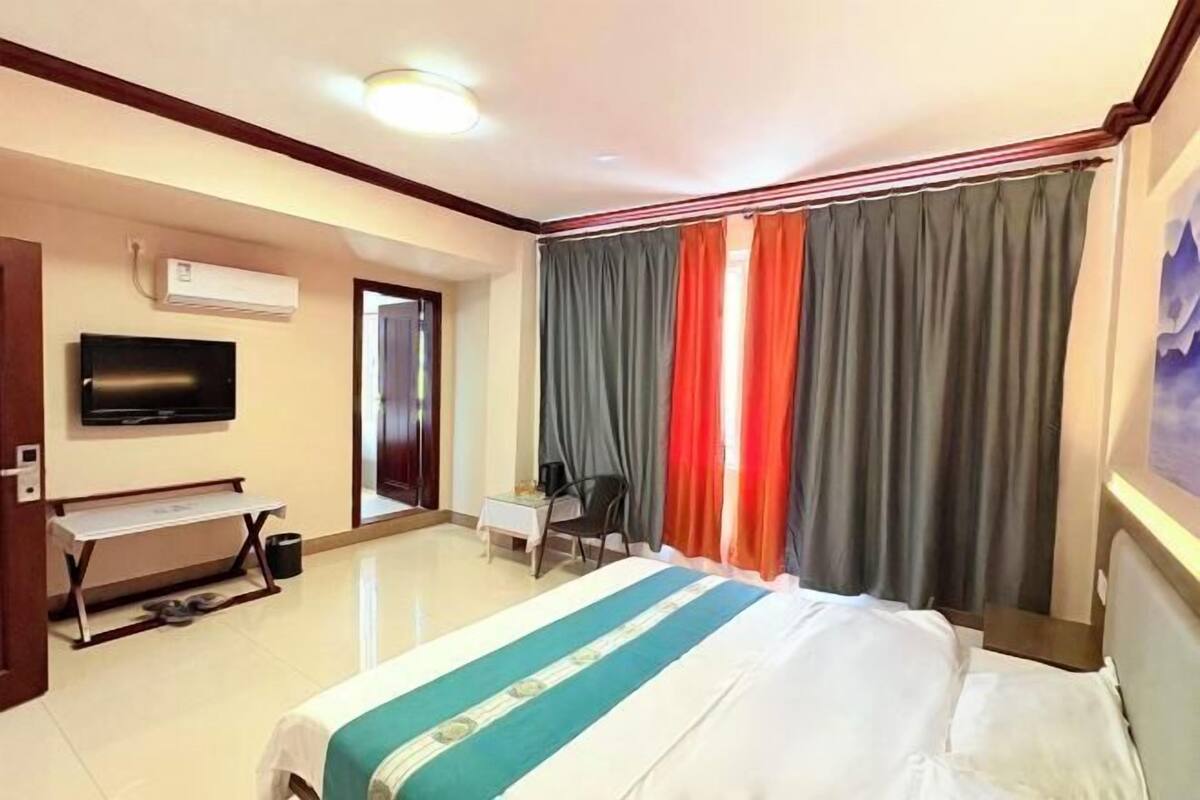 A hotel room with a bed, a desk, a chair, a television, and a window with curtains.