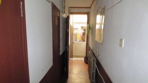 A narrow hallway with wooden flooring and white walls, leading to a room with a window and a radiator.