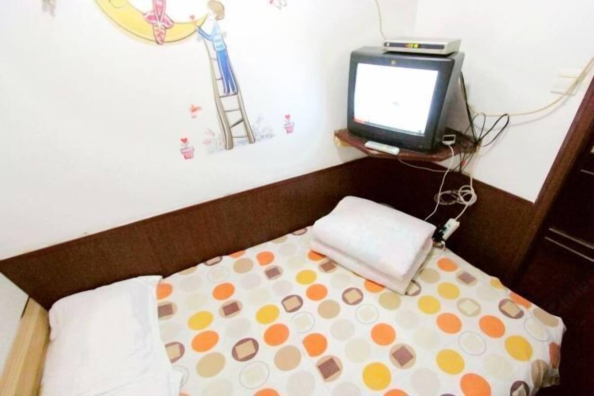 A bedroom with a bed, a television on a stand, and a wall decal.