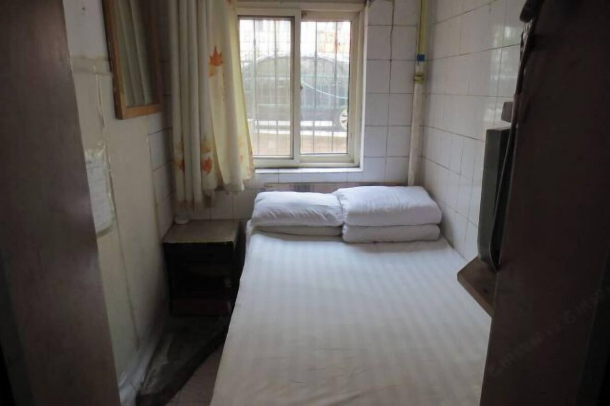 A small, narrow room with a single bed, a window with curtains, and a tiled wall.
