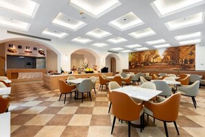 Un'ampia sala da pranzo con numerosi tavoli e sedie, un bancone centrale e un grande murale a parete.