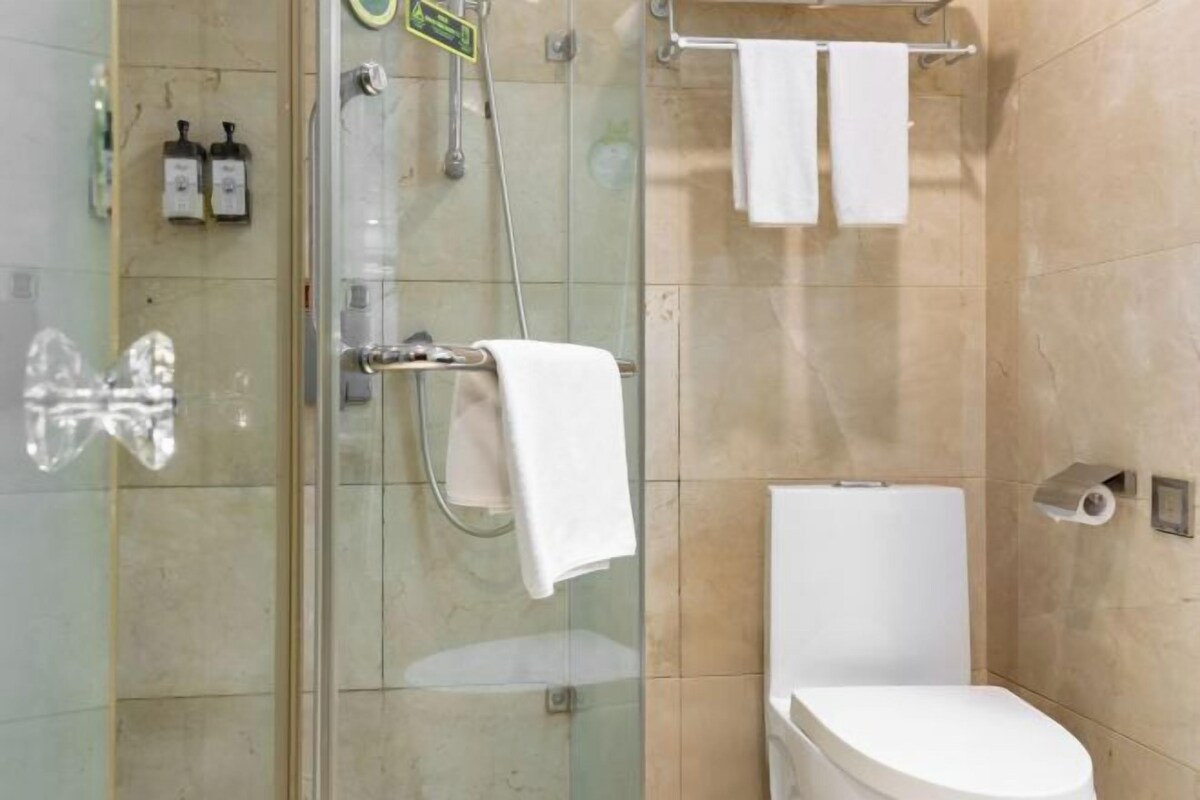 A bathroom with a glass shower enclosure, a white toilet, and two white towels hanging on a rack.
