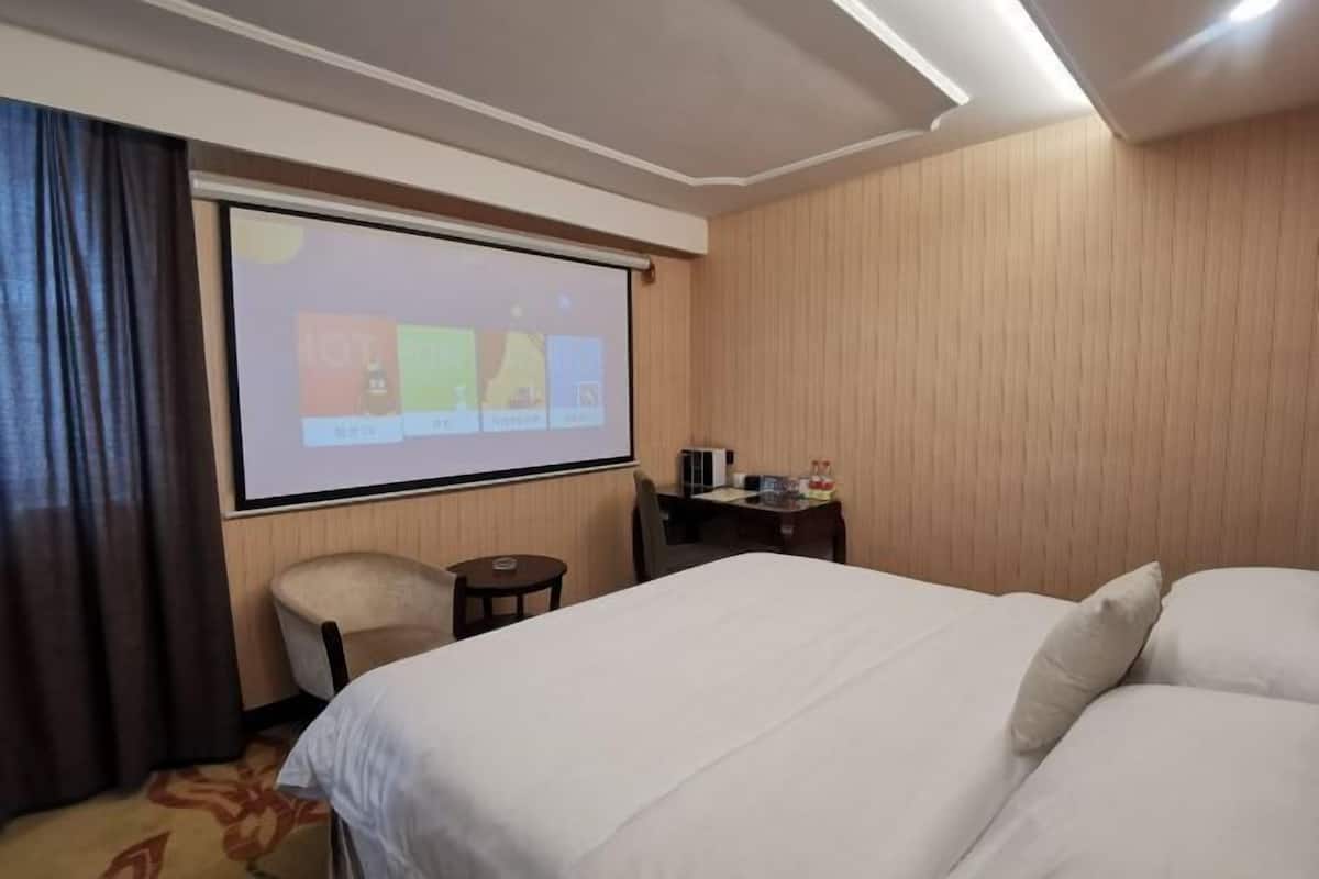 A hotel room with a bed, a desk, a chair, a projector screen, and a wooden wall.
