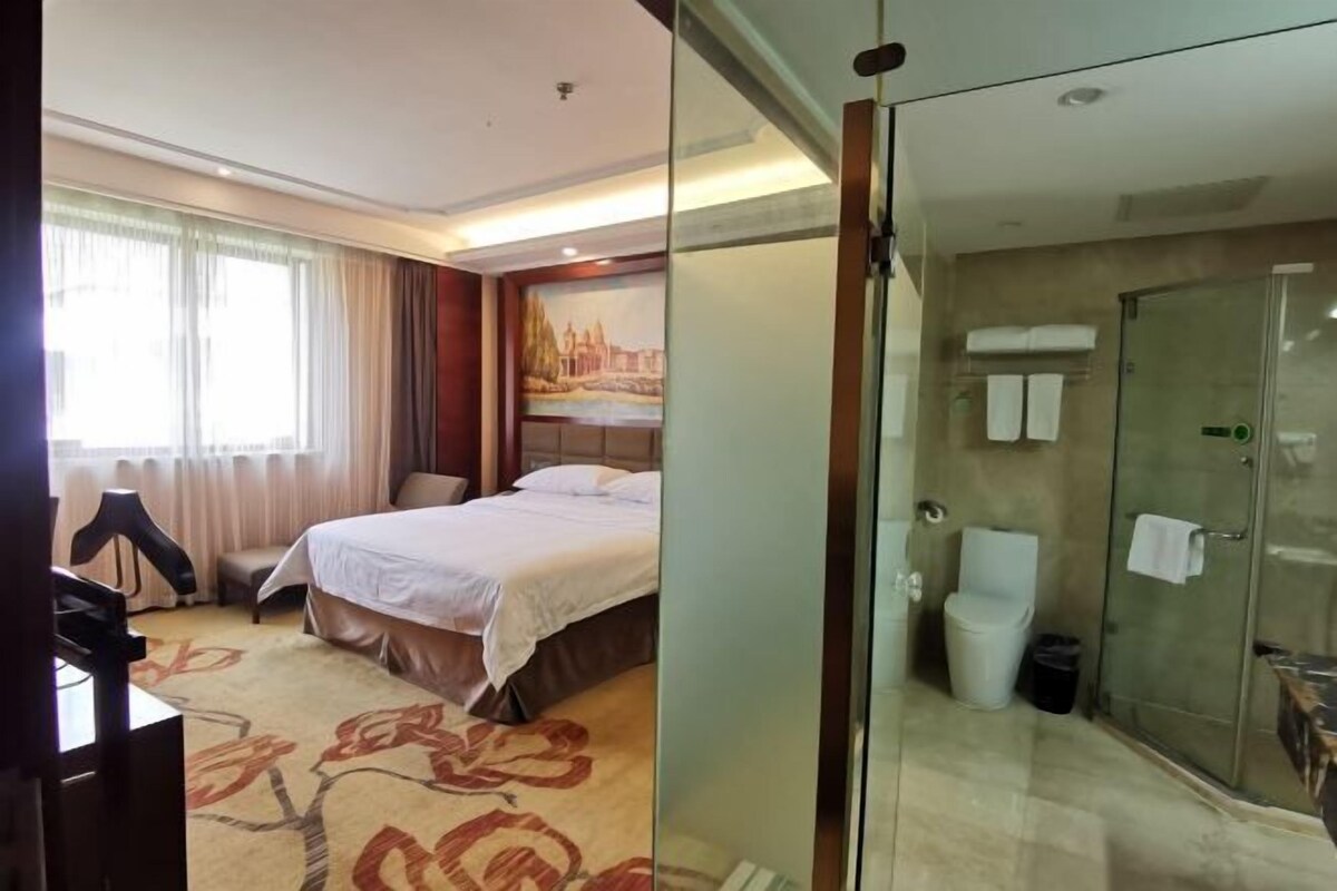 A hotel room with a bed, a desk, a chair, a shower, and a toilet.
