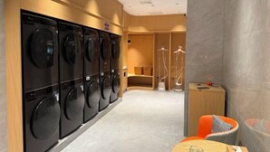 Una lavanderia moderna con diverse lavatrici, un angolo relax con un tavolo e un locale spogliatoio con specchio e porta asciugamani.