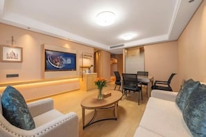 Quarto de hotel moderno com sofá, mesa de centro, televisão e escrivaninha com cadeiras.