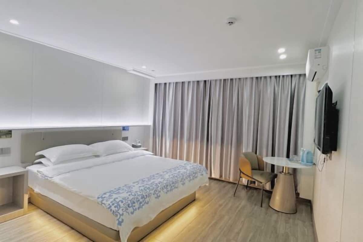 A modern hotel room with a large bed, a bedside table, a chair, a small round table, and a TV mounted on the wall.