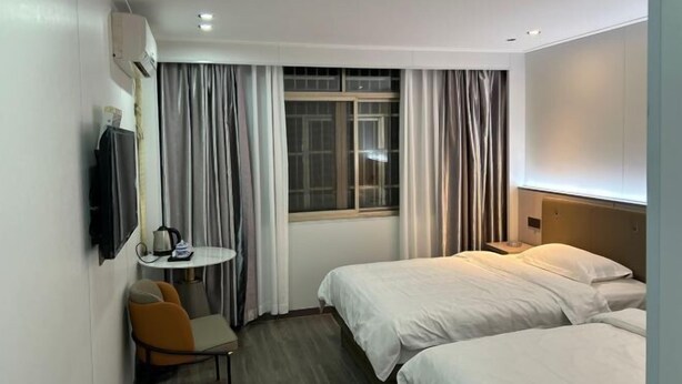 Habitación de hotel con dos camas, una mesita con un hervidor, una silla y un televisor montado en la pared.