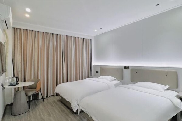 A hotel room with two beds, a small table with a chair, a wall-mounted air conditioner, and a curtain.