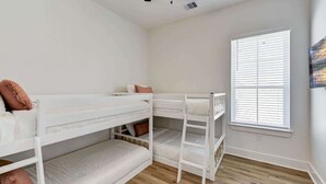 Une chambre avec des lits superposés, une fenêtre avec des stores et un ventilateur de plafond.