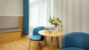A room with a blue chair, a round wooden table with a vase of flowers, and a bookshelf with books. - Super 8 Shanghai Dongjing Huanlegu Dongye Road (Shanghai)