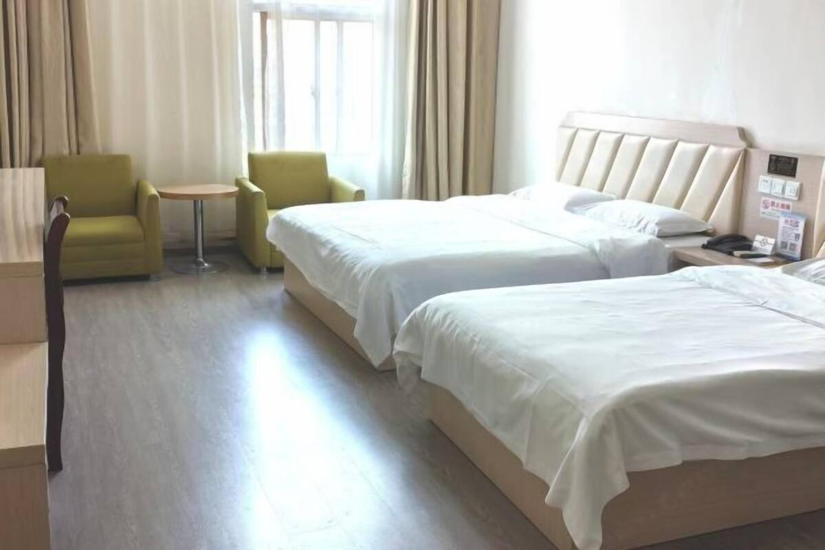 A hotel room with two beds, a small table, two chairs, and a coat rack.