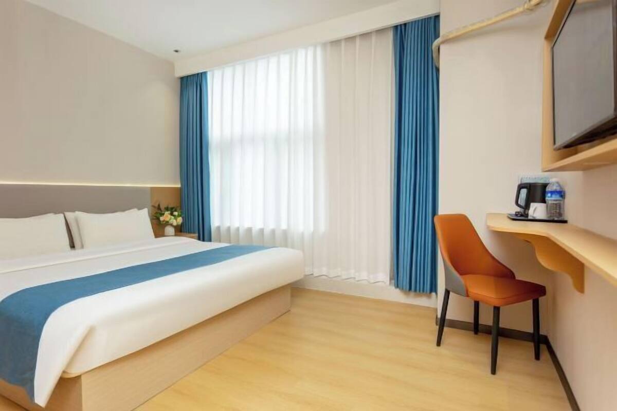 A hotel room with a bed, a desk with a chair, a television, and a window with curtains.