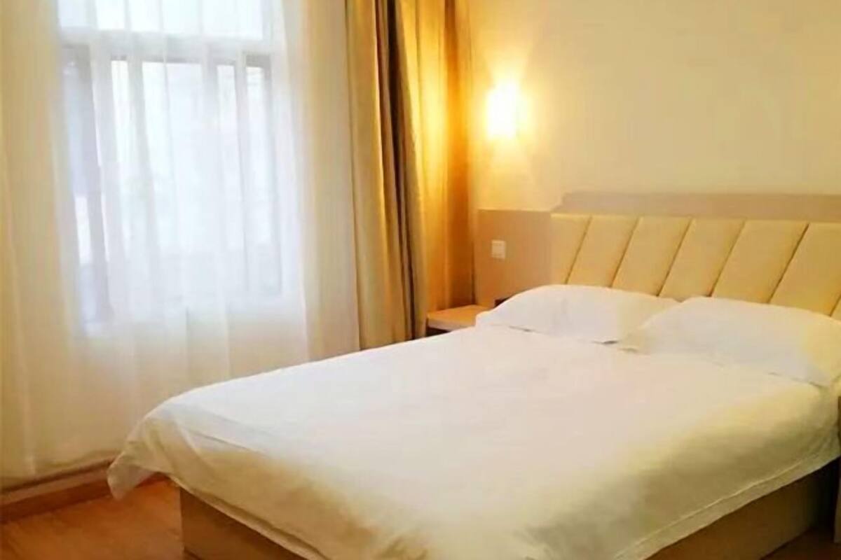 A hotel room with a bed, a nightstand, and a window with sheer curtains.