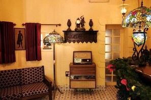Een gezellige woonkamer met een gestreept sofa, een vintage radio, een decoratieve lamp en een wandplank met beeldjes.