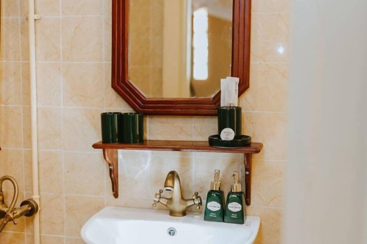 Un baño con repisa de madera que sostiene artículos de tocador, un grifo dorado y un espejo sobre el lavamanos.