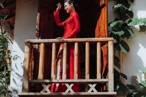 A person in red attire standing on a balcony with a wooden railing. - Ngoi Lang CO 77 Hoang Dieu (Dalat)