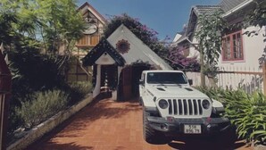 Un VUS blanc était garé dans une allée menant à une maison de style architectural traditionnel, avec notamment un toit à pignon et une porte d’entrée décorative.