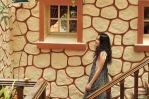 A person standing in front of a stone building with a window and a staircase. - Ngoi Lang CO 77 Hoang Dieu (Dalat)