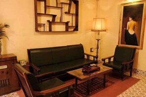 A room with a green sofa, two wooden chairs, a small table, a lamp, and a painting on the wall. - Ngoi Lang CO 77 Hoang Dieu (Dalat)